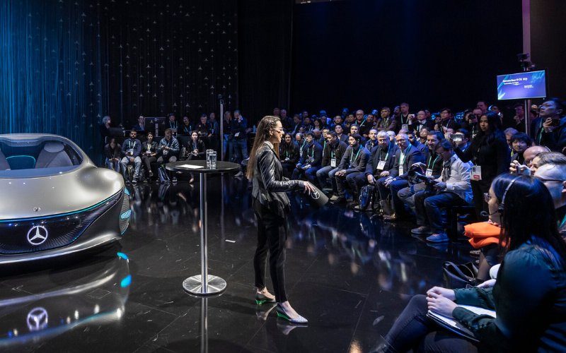 AI keynote speaker Katie Linendoll presenting beside a concept vehicle to an engaged crowd